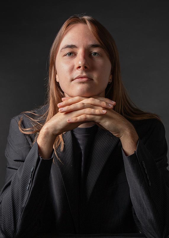 Portait of a young man in a dark blazer crossing his hands under his chin