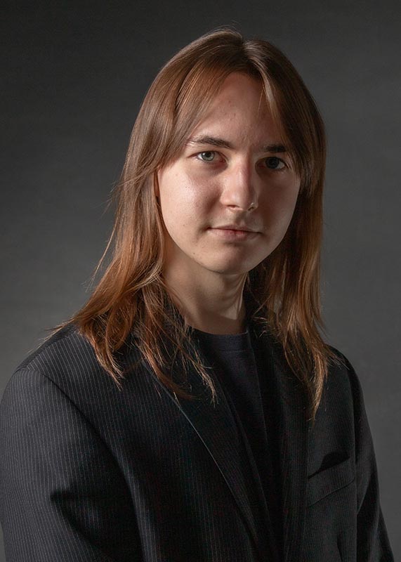 Portrait of a young man in a dark blue blazer looking at the camera with a light smile on his face