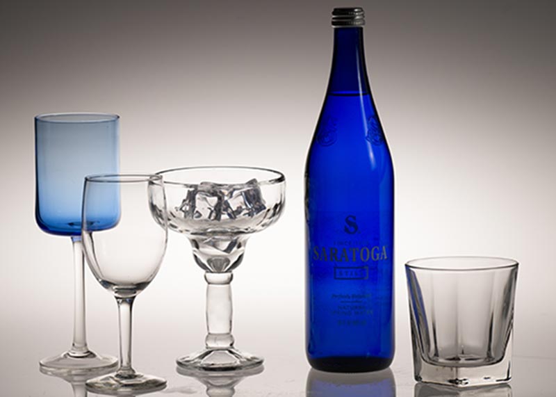 Still Photograph of a blue water bottle with different shapes and sizes of clear glasses
