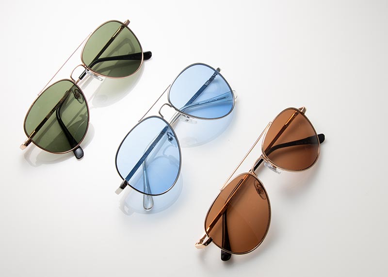 Three pairs of aviator glasses in blue, green and brown tint laying in descending order from the upper left to lower right corner