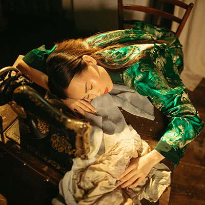 A woman sleeps at a vintage sewing machine.