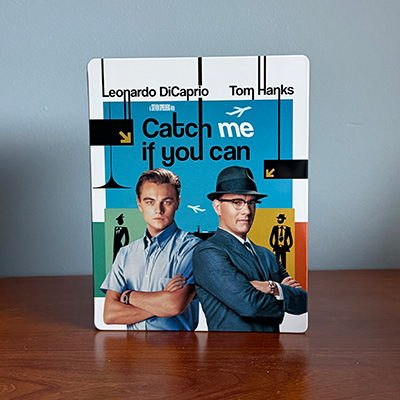 A Steelbook with two men pictured crossing their arms, with their backs against eachother, accompanied with background art with limited colors