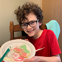 Image of male child smiling holding a cookie on a plate