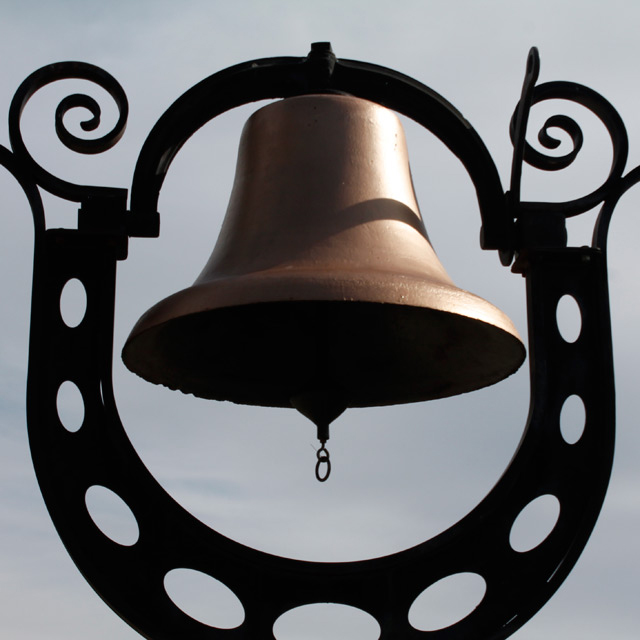 A close-up of big metallic bell with a gray sky background.