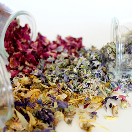 a variety of dried flower petals slightly poured out of jars, laying on a table