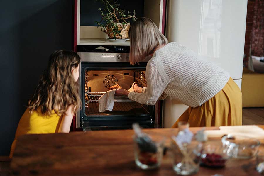 A woman and child putting a cake into the oven