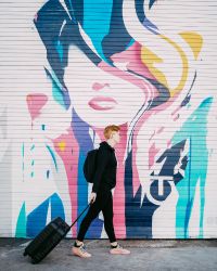 red haired person walking with a suitcase in front of wall art