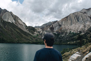 A man close up, wandering along a along that is framed all around by large, jutting mountains.