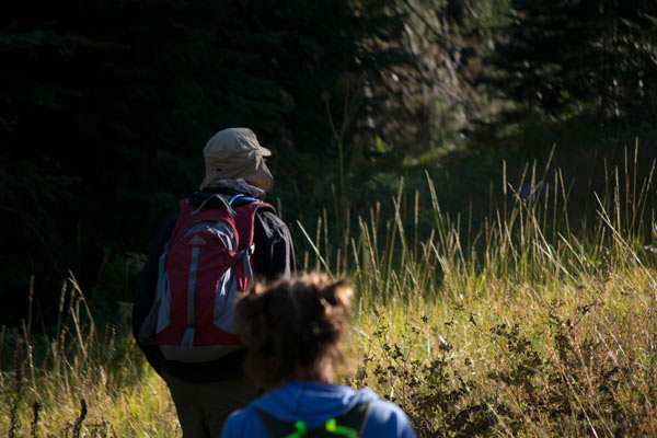 A young woman, slightly blured in the foreground, with another college age man wandering along a trail in the center of the image. 