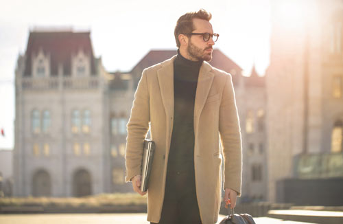man carrying a laptop wearing a nice coat ajd looking into the distance